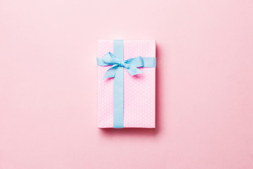 Gift box with blue bow for Christmas or New Year day on pink background, top view with copy space