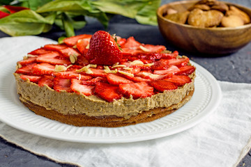 Vegan Strawberry Cake. Homemade cake with raw cream of dates and coconut milk, without eggs and gluten on almond flour on a white plate on a dark table. The concept of proper nutrition, sweets without