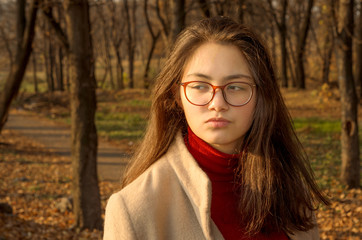 A young girl in a light coat and Burgundy turtleneck on a walk in the Park. Close up. Selective focus.