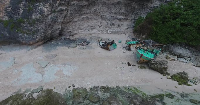 Big wreckage of a blue boat on the beach of Bali, a little boy is throwing rocks