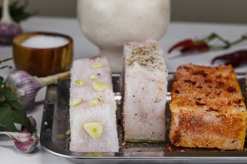 Three large pieces of salted lard with garlic, paprika and black pepper lie on a metal tray