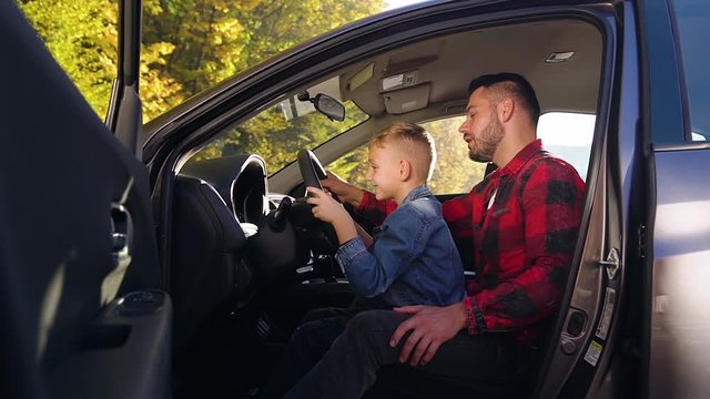 Side view of handsome bearded man which sitting with his nice son on the front seat and teaching to drive