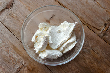Homemade cottage cheese in a glass bowl on old wooden table background closeup. Top view