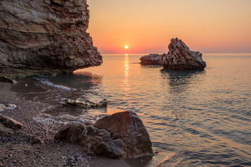 the sun rising over the sea in the early morning rocks and stones in the water a Sunny path