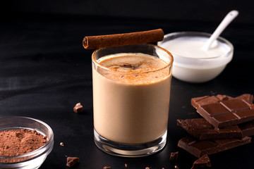lassi indian chocolate drink on a black background next to the ingredients with yogurt, cocoa and chocolate