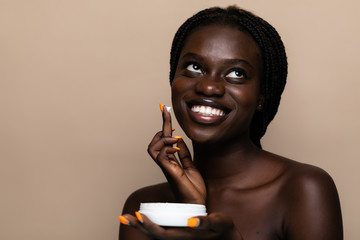 Young african american beauty using face cream isolated on beige background
