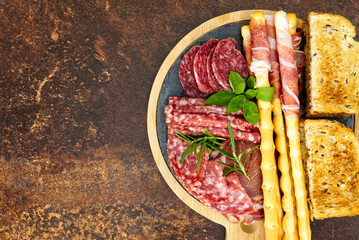 Meat and cheese plate antipasti snack with Prosciutto ham, Parmesan, Blue cheese, Cantaloupe melon and Olives on olive wood serving board on dark stone background