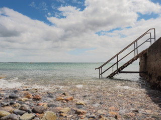Fototapeta na wymiar Blue ocean water and cloudy sky, Old metal stairs from a pier. Nature background.