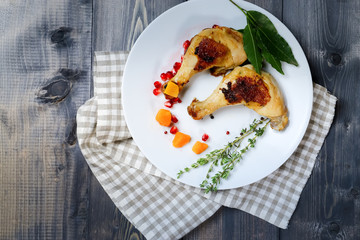 On a dark tabletop on a linen checkered napkin, mint twigs lie and there is a white dish with two fried legs