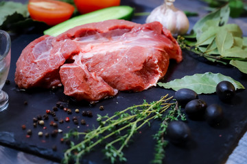On a dark countertop, a large piece of raw beef, garnished with bay leaves, pepper