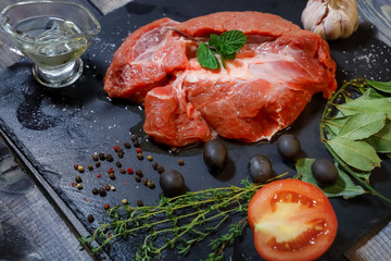 On a dark countertop, a large piece of raw beef, garnished with bay leaves, pepper