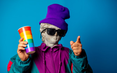 antique statue dressed in trendy clothes of the nineties holds cup of drink