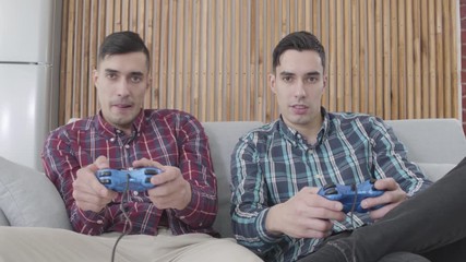 Portrait of happy adult Caucasian men playing video games. Smiling twin brothers giving high five as winning in competition. Leisure, lifestyle, happiness.