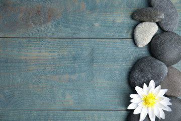 Fototapeta na wymiar Stones with lotus flower and space for text on blue wooden background, flat lay. Zen lifestyle