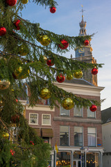 Closeup of red and yellow Christmas balls on the branches of a Christmas tree with the tower of the Sint Janskerk of Gouda in the background. The Netherlands, Europe.