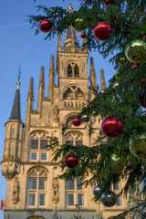 Closeup of red and yellow Christmas balls on the branches of a Christmas tree with the old town hall of Gouda in the background. The Netherlands, Europe.