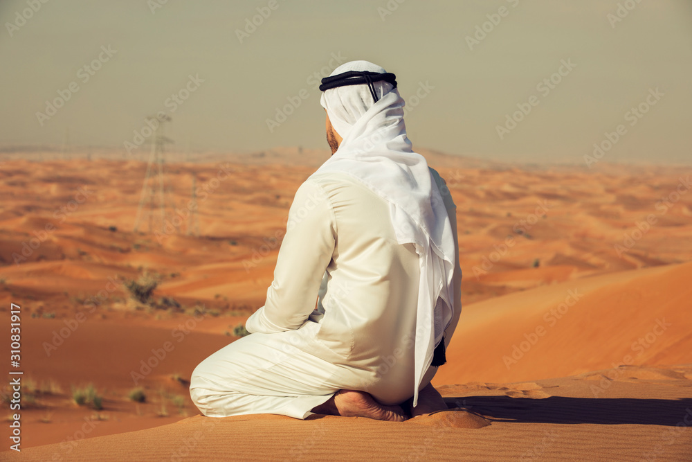 Wall mural Arab Emirati man sitting on top of a dune in UAE desert - Wall murals