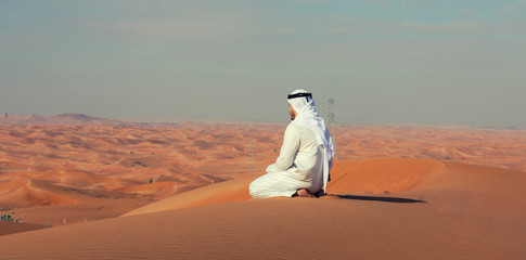 Fototapeta premium Arab Emirati man sitting on top of a dune in UAE desert