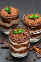 Classic tiramisu dessert in a glass cup and pieces of chocolate on dark concrete background