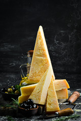 Parmesan. Pieces of Parmesan cheese on black stone background. Top view. Free space for your text. - obrazy, fototapety, plakaty