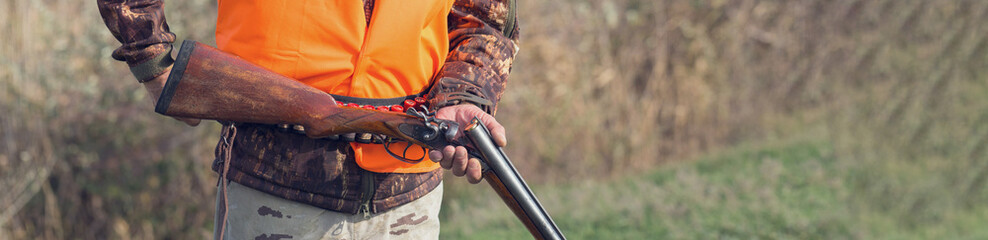 A man with a gun in his hands and an orange vest on a pheasant hunt in a wooded area in cloudy...
