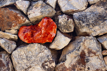 Red heart of stone among old stones, texture, background.