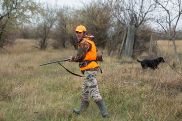A man with a gun in his hands and an orange vest on a pheasant hunt in a wooded area in cloudy...