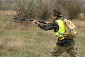 Hunting period, autumn season open. A hunter with a gun in his hands in hunting clothes in the autumn forest in search of a trophy. A man stands with weapons and hunting dogs tracking down the game.