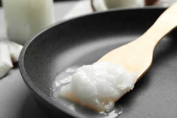 Frying pan with coconut oil and wooden spatula on grey table, closeup. Healthy cooking