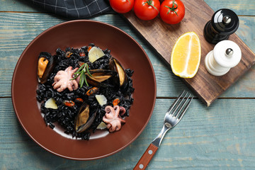 Delicious black risotto with seafood served on blue wooden table, flat lay
