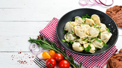 Russian pelmeni meat Dumplings with greens in a black plate. Russian traditional cuisine. Top view. Free copy space.