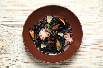 Delicious black risotto with seafood on white wooden table, top view