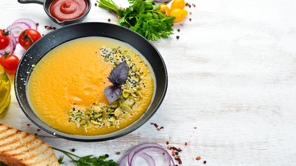 Pumpkin soup with pumpkin seeds in a black plate on a white wooden background. Top view. Free space for your text.