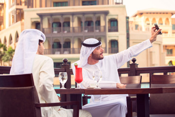 two Arab man taking a selfie in a cafe, and drink red juice at Dubai in evening