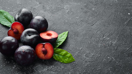 Fresh plums with leaves on a black stone table. Top view. Free space for your text.