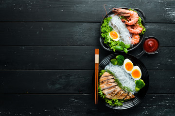 Rice noodles dishes in black plate on black background. Asian cuisine. Top view. Free space for your text.