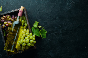 Bottle of white wine and fresh grapes on a black stone table. Top view. Free space for your text.