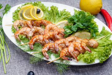 King prawns on a lettuce leaf on a white plate. Decorated with lemon, olives and parsley.