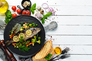 Baked trout fish with vegetables and lemon on a black plate. Top view. Free copy space.