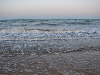Natural picture of coastal sea waves foaming on an evening sandy beach.