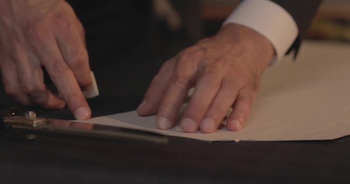 Footage of a tailor drawing lines on fabric and making some alterations arround the cut with his chalk-flat profile