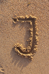 Alphabet (j) letters handwritten in sand on beach