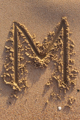 Alphabet (m) letters handwritten in sand on beach