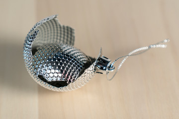 Broken shiny gray christmas ball with cracks and splinters on a wooden table