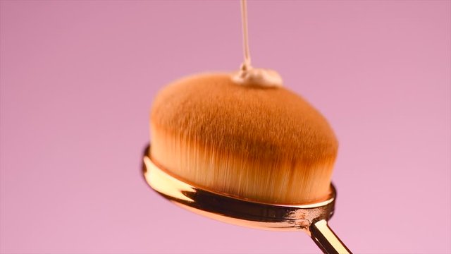 Make-up liquid foundation pouring on makeup brush, closeup. Foundation beauty facial cosmetics, toothbrush brush tool for perfect make up. Dripping bb cream or concealer, on pink background. 4K slowmo