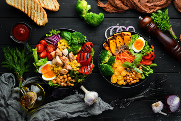 Buddha bowl: vegetables, fruits and meat in black plate on old background. Autumn dishes. Top view. Free space for your text.
