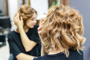 Beautiful woman is touching her hair, checking her hairstyle in the mirror at beauty salon, copy...