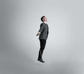 Fototapeta na wymiar Back in childhood. Feels like free bird. Man in office clothes training with jumping rope on grey background. Unusual look for businessman in motion, action. Sport, healthy lifestyle, working.