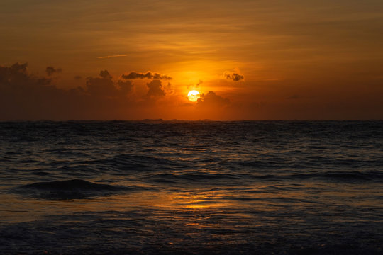 Sunrise over the ocean. The sun rises above the horizon through the clouds and paints the sky a Golden color.