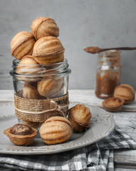 food photography of homemade hazelnut cookies with chocolate filling close-up in a glass jar side view on a gray texture background
